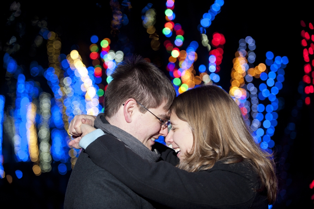 Engagement Photography - Couple nuzzling and smiling in front of Christmas lights