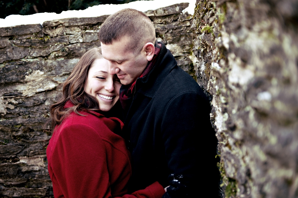 Engagement Photography - Winter couple embracing next to stone wall